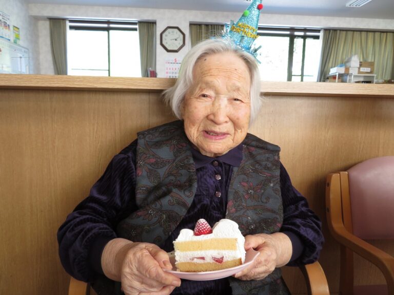 施設の誕生日会で笑顔でケーキを持つ入居者